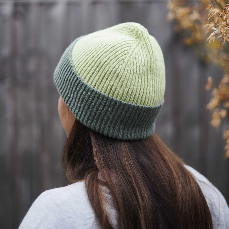 Person wearing a two-tone green and gray knit beanie outdoors.