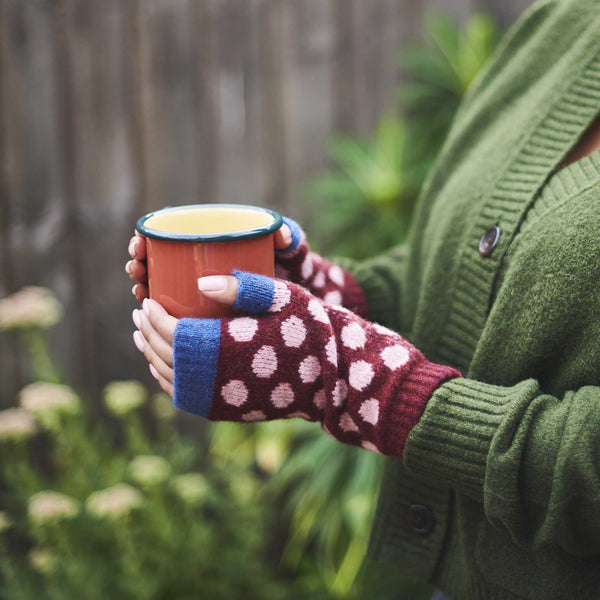 Person wearing a green sweater and polka dot gloves holding a red cup outdoors.