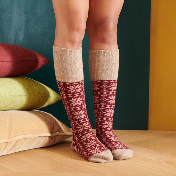 Person wearing red and beige patterned knee-high socks with a colorful pillow background