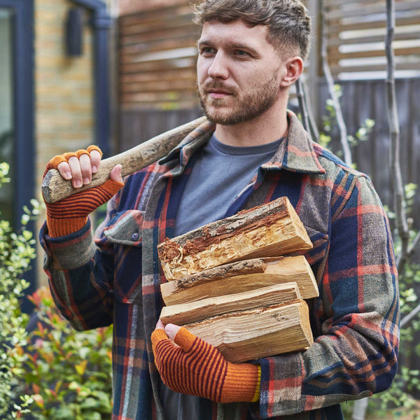 Man holding a bundle of firewood and an axe outdoors