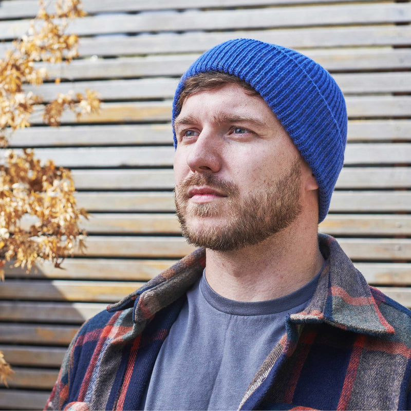 Man wearing a blue beanie and plaid jacket against a wooden background