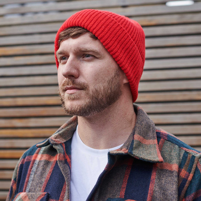 Man wearing a red beanie and plaid jacket against a wooden background