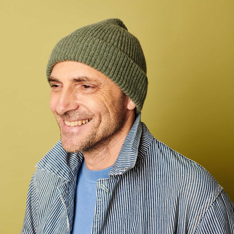 Man wearing a green beanie and striped jacket against a yellow background