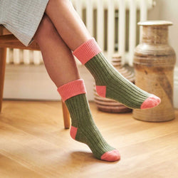 Green socks with pink accents worn by a person sitting on a wooden chair.