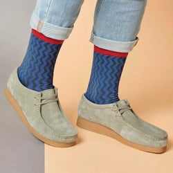Person wearing blue socks with red accents and light gray shoes on a beige background