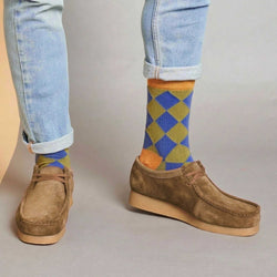 Person wearing blue jeans and brown shoes with colorful argyle socks on a neutral background