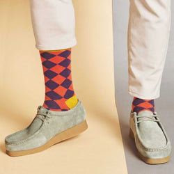 Colorful checkered socks worn with light gray shoes on a two-tone background