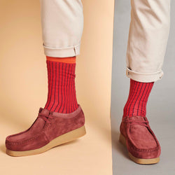 Red suede shoes worn with red striped socks on a beige and gray background