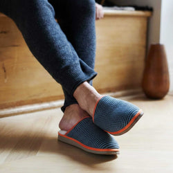 Person wearing blue slippers with orange accents on a wooden floor.