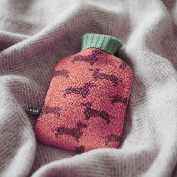 Pink hot water bottle with dog pattern on a soft fabric background