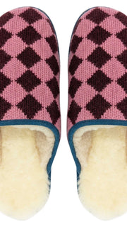 A pair of Catherine Tough knit slip-on slippers with a pink and dark burgundy argyle pattern, featuring a cream-colored sheepskin lining and a blue trim along the edge.