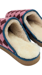 A pair of Catherine Tough knit slip-on slippers with a pink and dark burgundy argyle pattern, featuring a cream-colored sheepskin lining and a blue trim along the edge.